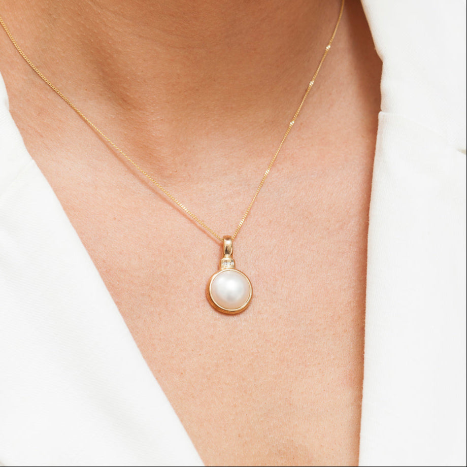 The Margaret Enhancer is the epitome of timeless elegance, featuring a luminous white Mabe cultured pearl with a flawlessly smooth, creamy surface. Set in a sleek diamond-accented bail, this exquisite enhancer adds a touch of refined luxury to any look. Its minimalist yet striking design makes it the perfect piece for effortless, everyday sophistication. 