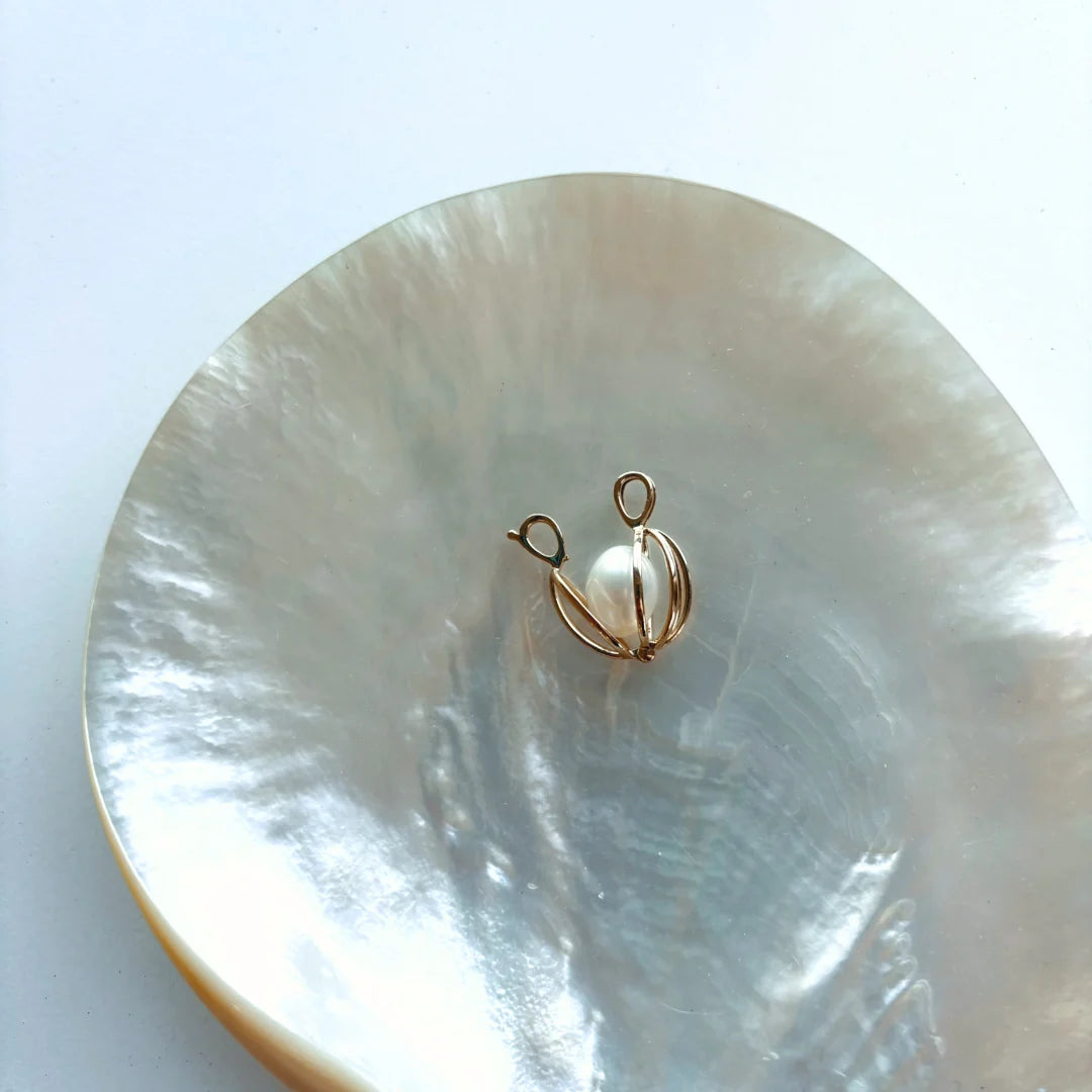 Timeless and sophisticated, the Celia Pendant features an openable 9ct yellow gold cage designed to showcase a white Freshwater pearl. The polished structure frames the pearl beautifully, allowing its natural lustre to shine from every angle.

Its hinged opening allows you to easily interchange the pearl, offering versatility for every occasion. A delicate and refined piece for lovers of classic pearl jewellery.