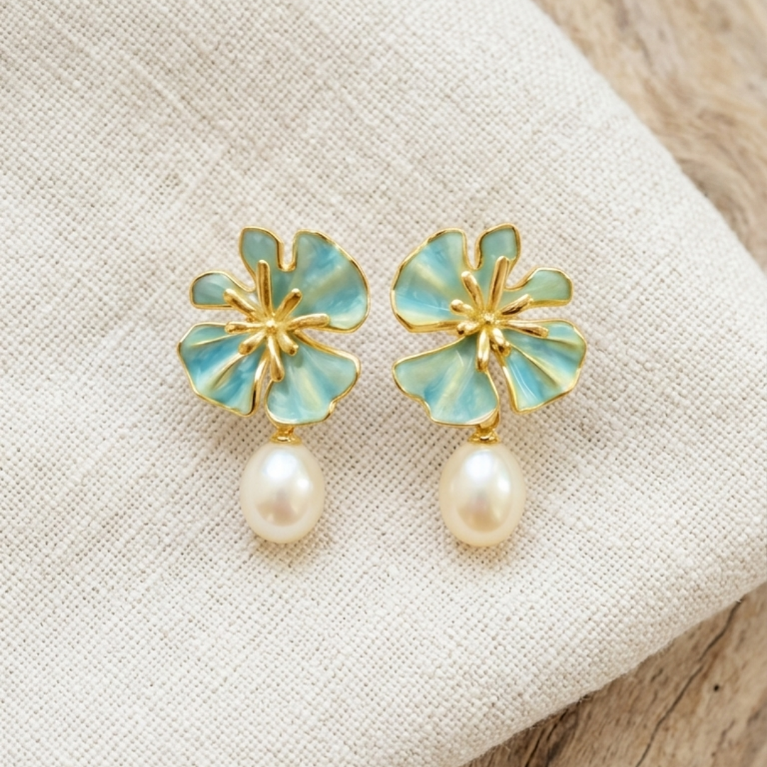 The Posie Earrings are a joyful expression of colour and craftsmanship, crafted in sterling silver with warm yellow gold plating and finished with delicate enamel petals in a soft blush or blue tone. Inspired by blooming florals, each earring is accented with a luminous white freshwater pearl that catches the light with a gentle, natural glow. The combination of soft colour, golden warmth, and organic form creates a look that feels both playful and refined, balancing timeless pearl elegance with a fresh, mo