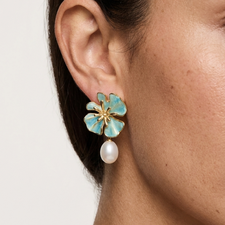 The Posie Earrings are a joyful expression of colour and craftsmanship, crafted in sterling silver with warm yellow gold plating and finished with delicate enamel petals in a soft blush or blue tone. Inspired by blooming florals, each earring is accented with a luminous white freshwater pearl that catches the light with a gentle, natural glow. The combination of soft colour, golden warmth, and organic form creates a look that feels both playful and refined, balancing timeless pearl elegance with a fresh, mo