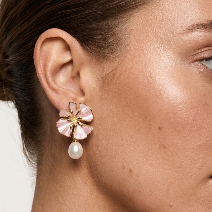 The Posie Earrings are a joyful expression of colour and craftsmanship, crafted in sterling silver with warm yellow gold plating and finished with delicate enamel petals in a soft blush or blue tone. Inspired by blooming florals, each earring is accented with a luminous white freshwater pearl that catches the light with a gentle, natural glow. The combination of soft colour, golden warmth, and organic form creates a look that feels both playful and refined, balancing timeless pearl elegance with a fresh, mo