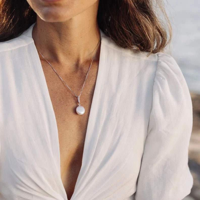 Presenting our Clarissa Pendant, an enchanting blend of sophistication and contemporary allure. Crafted from sterling silver, this pendant boasts sparkling cubic zirconias, complemented by a striking sizable coin-shaped freshwater pearl suspended below, adding an exquisite touch to any ensemble. Pair it with the Clarissa Earrings to curate a truly breathtaking combination.