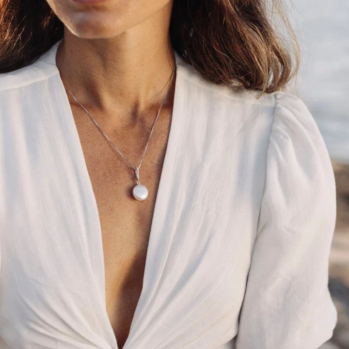 Presenting our Clarissa Pendant, an enchanting blend of sophistication and contemporary allure. Crafted from sterling silver, this pendant boasts sparkling cubic zirconias, complemented by a striking sizable coin-shaped freshwater pearl suspended below, adding an exquisite touch to any ensemble. Pair it with the Clarissa Earrings to curate a truly breathtaking combination.