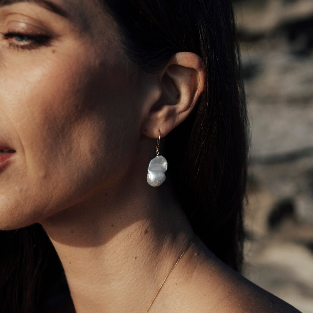The Alessia Hook Earrings are a refined expression of modern elegance, featuring a classic 9ct gold shepherd’s hook with a luminous baroque freshwater pearl delicately suspended below. Each pearl is naturally unique, with an organic shape that adds character and understated luxury to the design. Effortlessly wearable and beautifully balanced, these pearl drop earrings are the perfect finishing touch for both everyday outfits and special occasions.